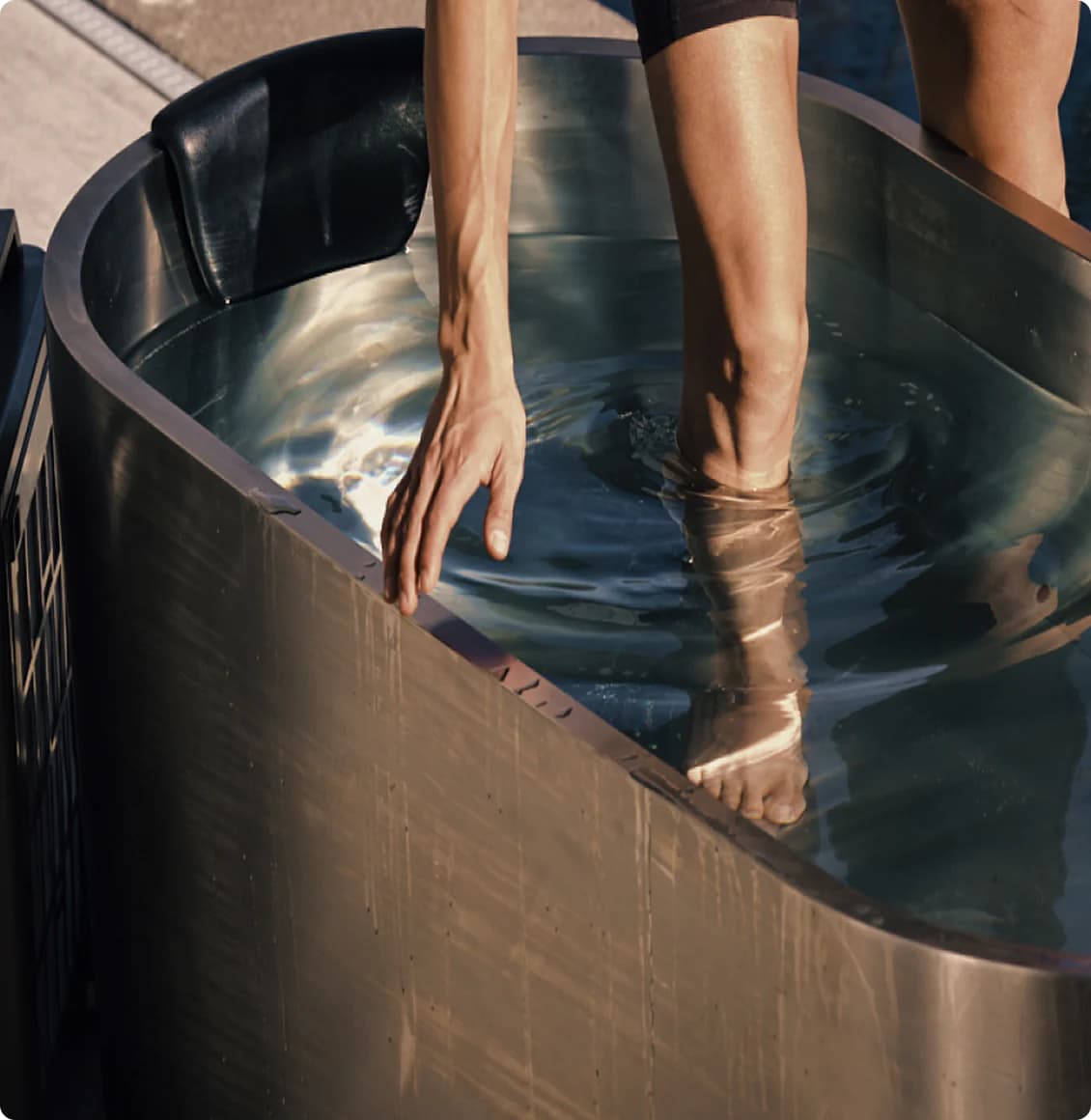 Close-up of a Polar Monkeys stainless-steel cold plunge as a person steps in, ripples spreading across sunlit water.