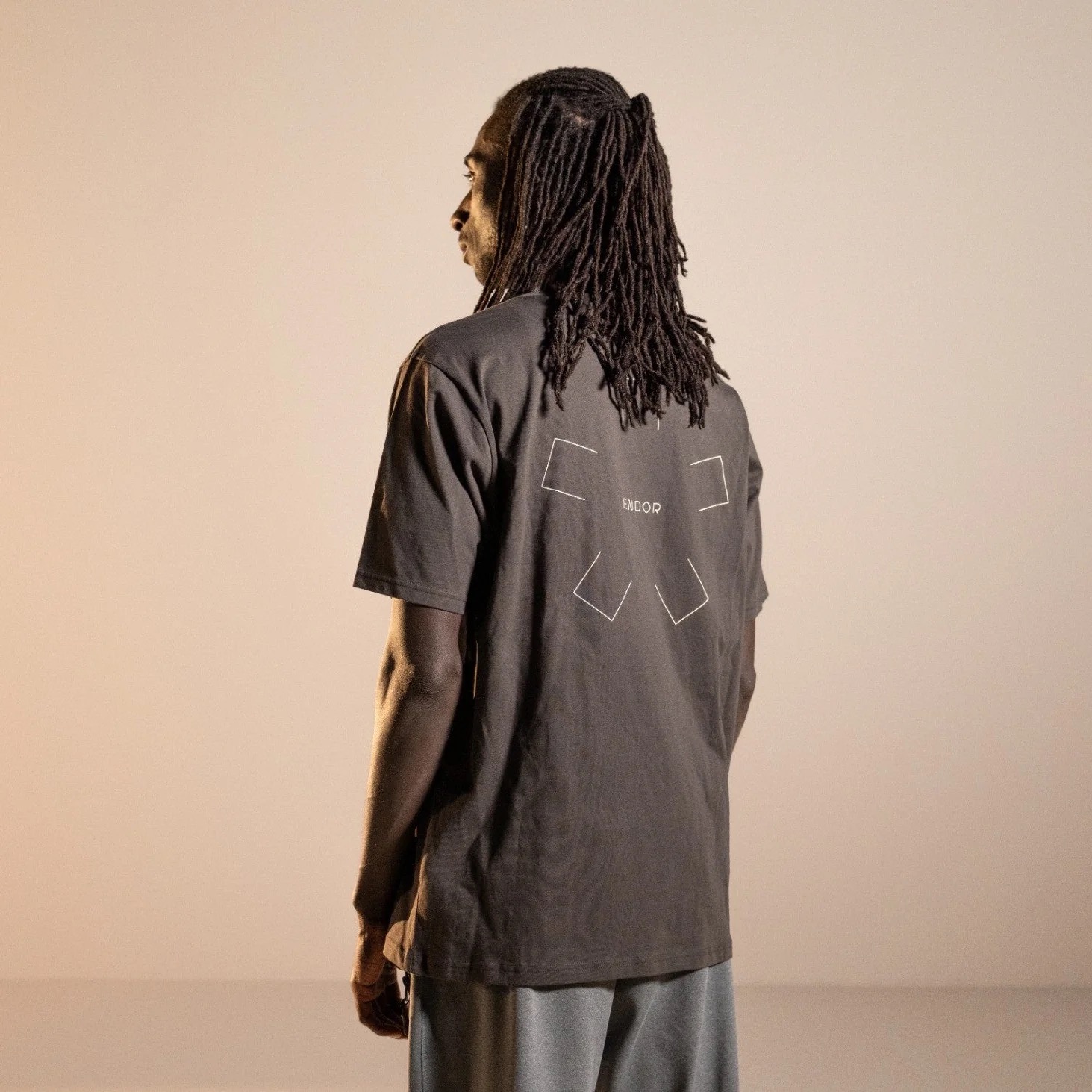 Figure from behind in a dark Endor t-shirt against a peach-pastel studio backdrop