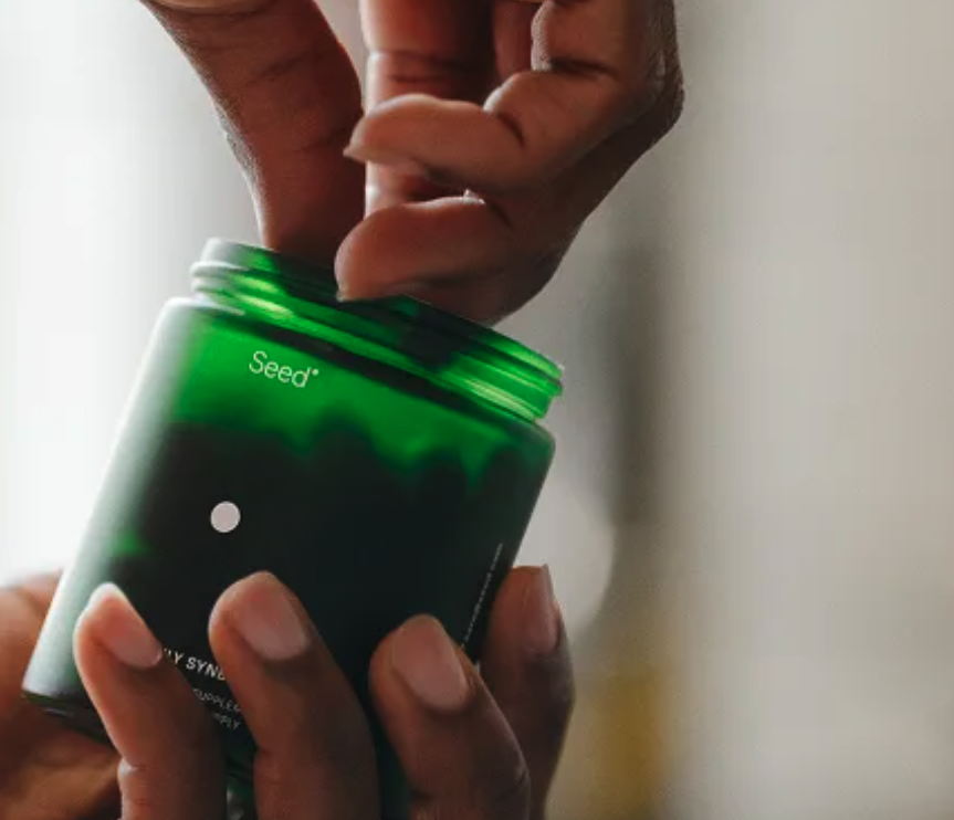 Hands opening a green Seed Daily Synbiotic jar