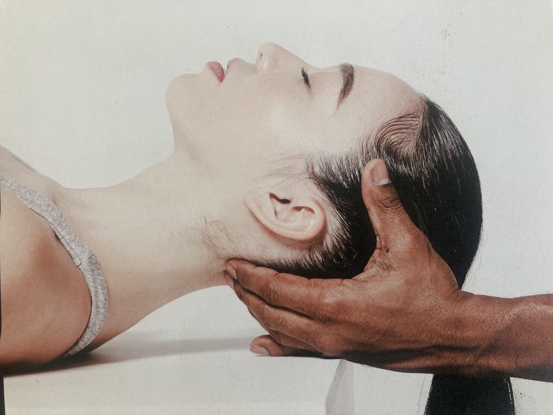 A Myodetox practitioner's hands cradling a reclining client's head and neck during a hands-on treatment session